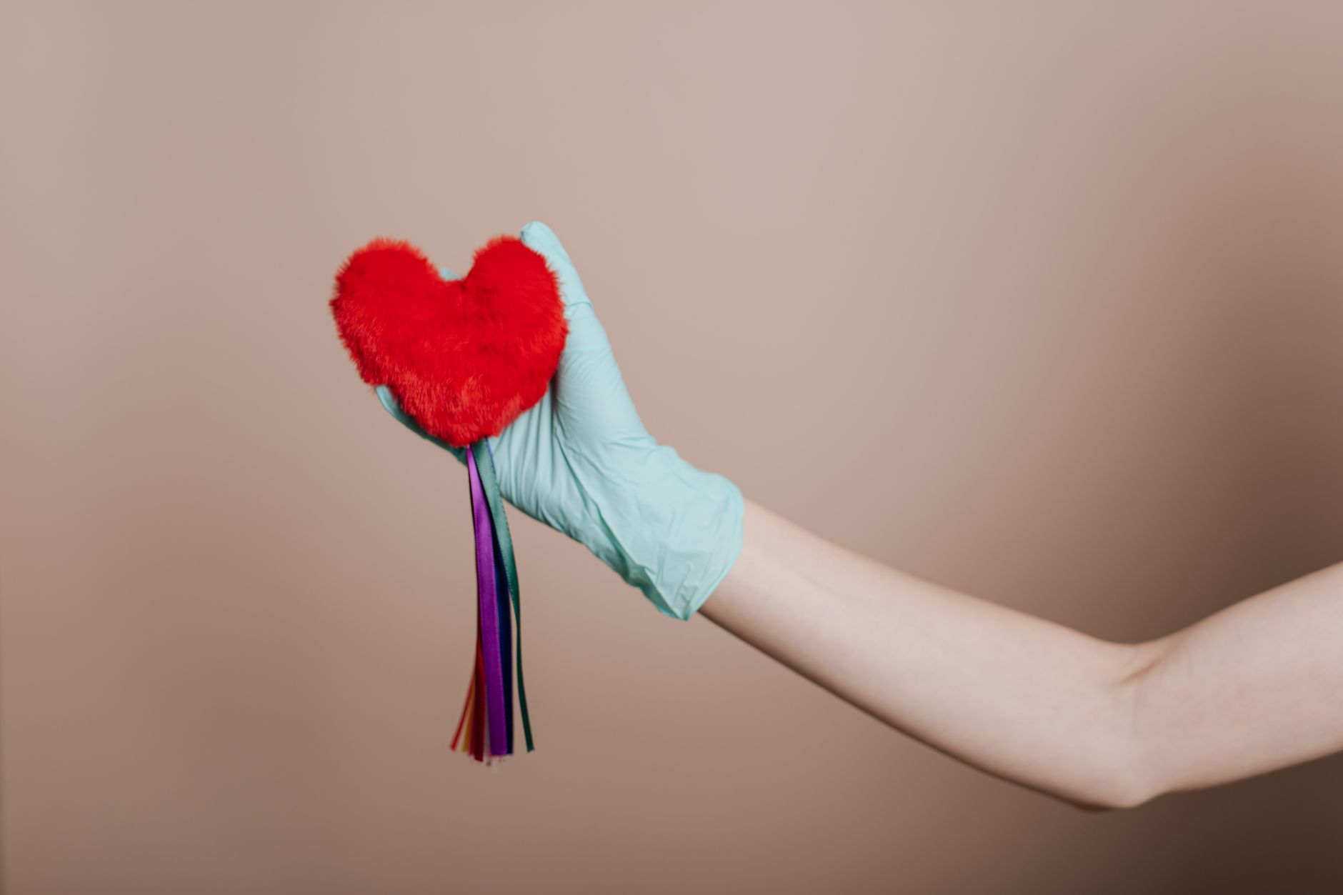 A latex-gloved hand holds a red heart-shaped plush with colorful strings, symbolizing love and safety. — The Ultimate Resourc